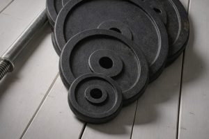 Svarta viktplattor och en skivstång på ett vitt trägolv.