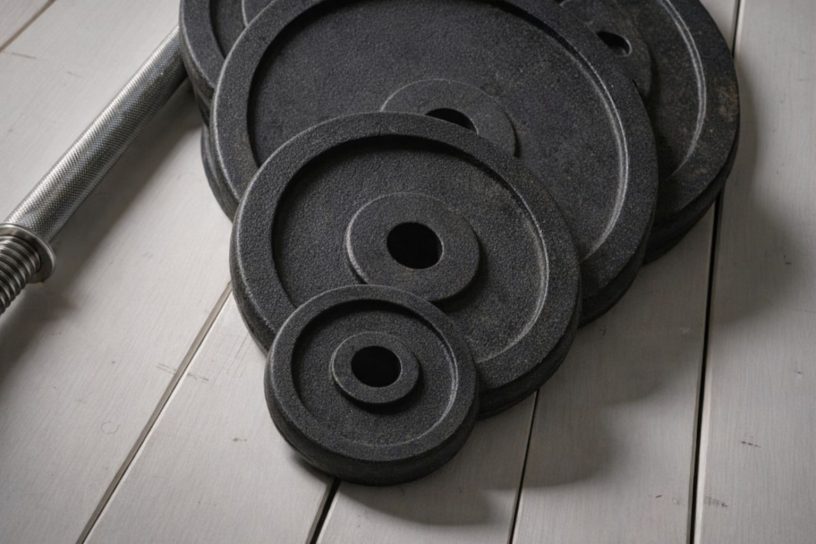 Svarta viktplattor och en skivstång på ett vitt trägolv.